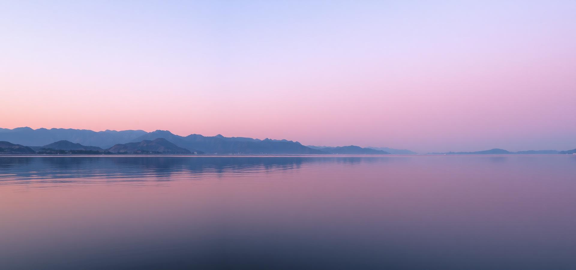 Un lago en calma al amanecer con montañas al fondo